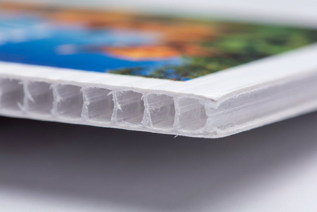 Close-up of a Corflute® board edge showing the hollow fluted polypropylene core under a full-colour print